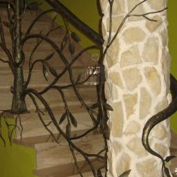 Zuh Metal-Plast - Kute balustrady schodowe w formie drzewa z liśćmi, oplatające kamienny filar, na tle zielonej ściany i marmurowych schodów.